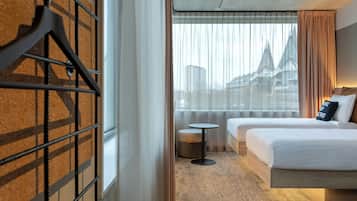 Habitación de hotel con dos camas, una mesita redonda y vista a un puente por la ventana.