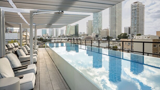 A rooftop infinity pool with lounge chairs, a clear view of the city skyline, and modern architecture. - Gymnasia Isrotel, A Tribute Portfolio Hotel (Tel Aviv)