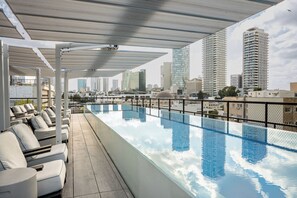 Ein Dachpool mit Infinity-Kante, Liegestühlen und freiem Blick auf den Stadtpanoramahimmel, ergänzt durch moderne Architektur.