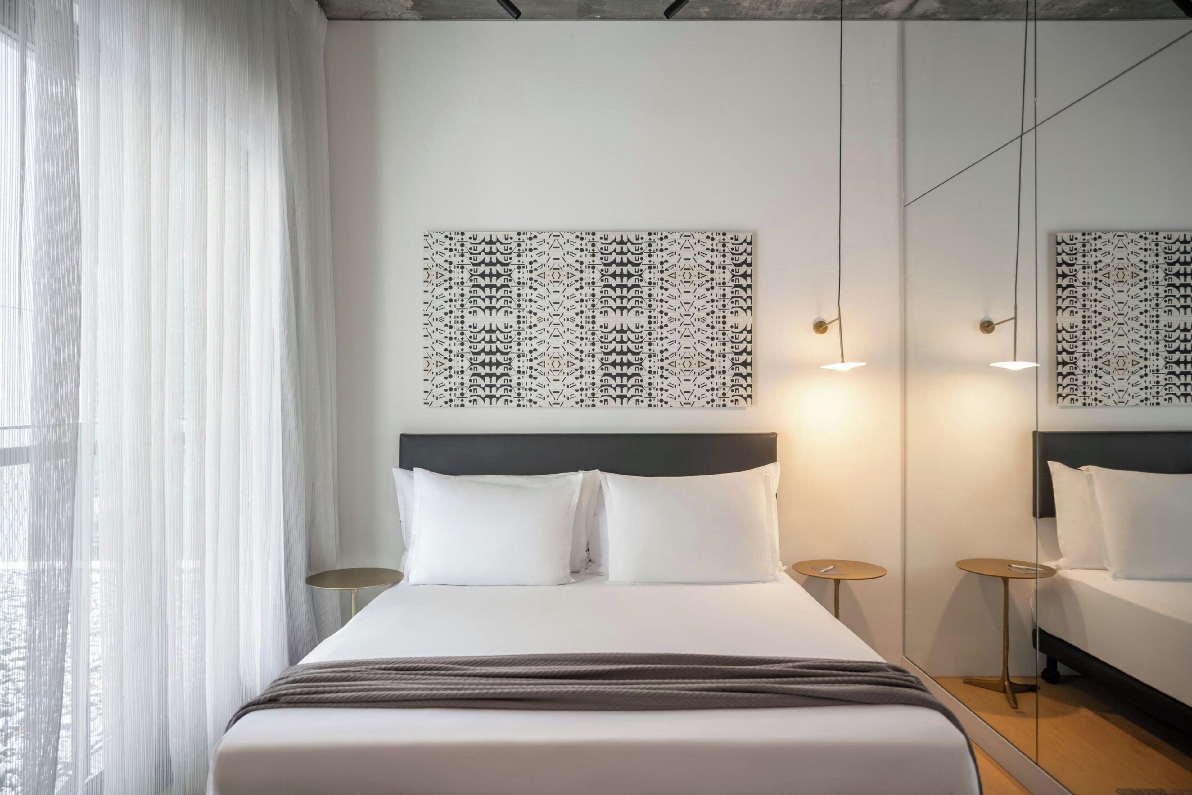 Een moderne hotelkamer met een groot bed, witte lakens, een donker hoofdeinde en een wandkunstwerk met een patroon erboven.