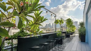 A rooftop bar with a city skyline view, featuring a row of black bar stools and potted plants. - Gymnasia Isrotel, A Tribute Portfolio Hotel (Tel Aviv)