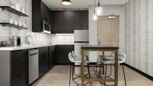 A modern kitchen with dark cabinets, stainless steel appliances, and a wooden dining table with bar stools. - Residence Inn By Marriott Yuma (Yuma)