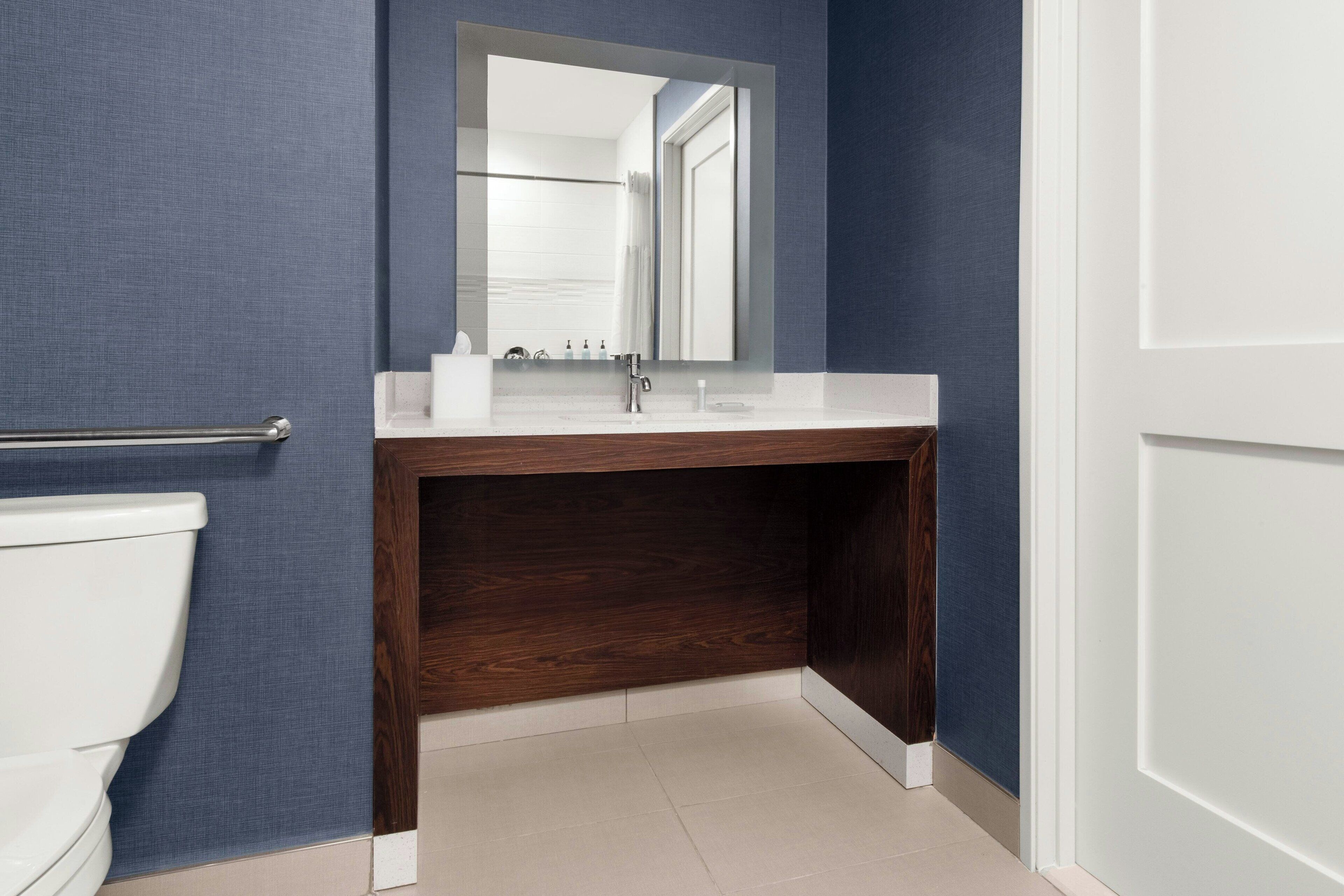 Un baño con inodoro blanco, tocador de madera con espejo y lavabo blanco.