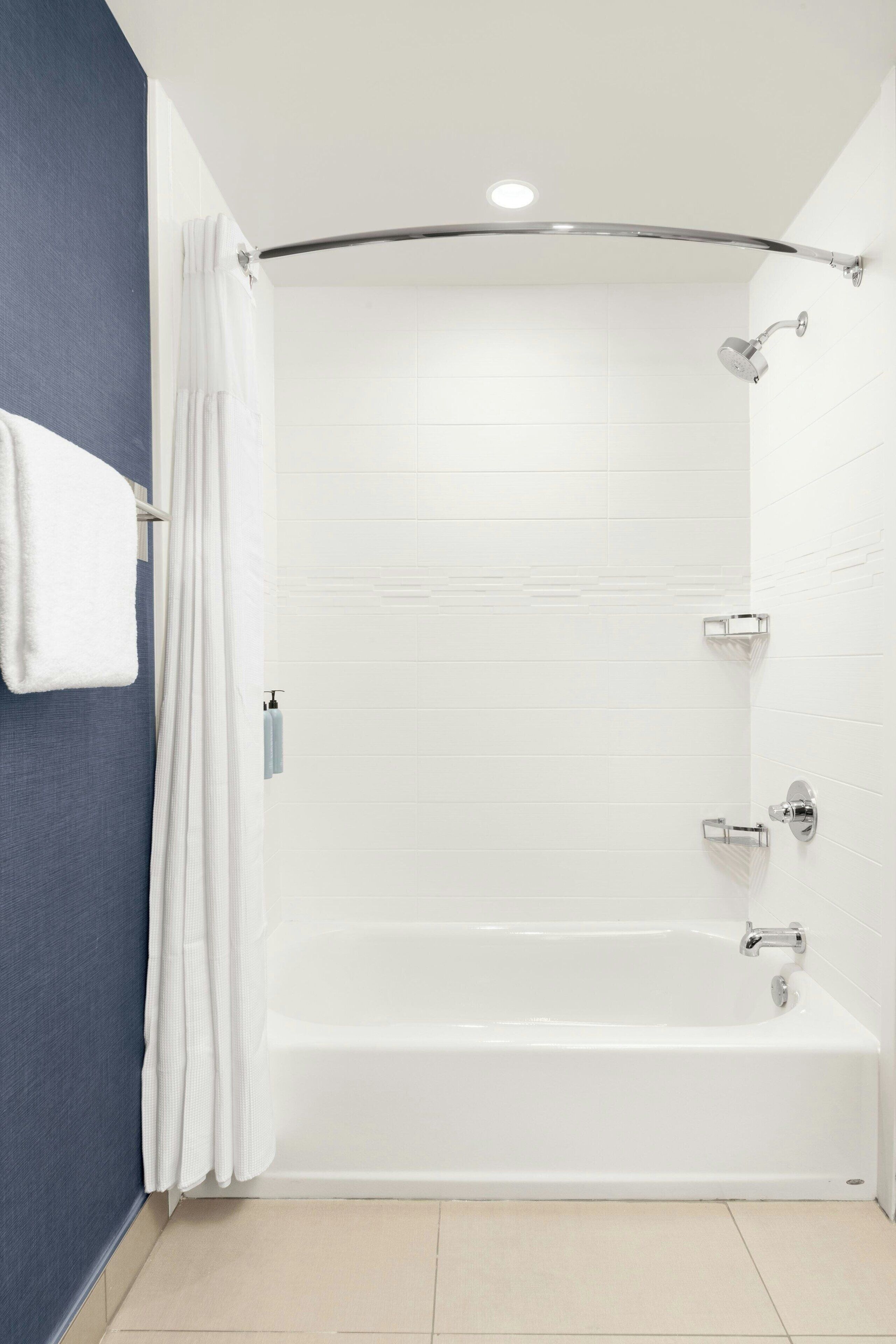 A modern bathroom with a white bathtub, a showerhead, and a towel rack.