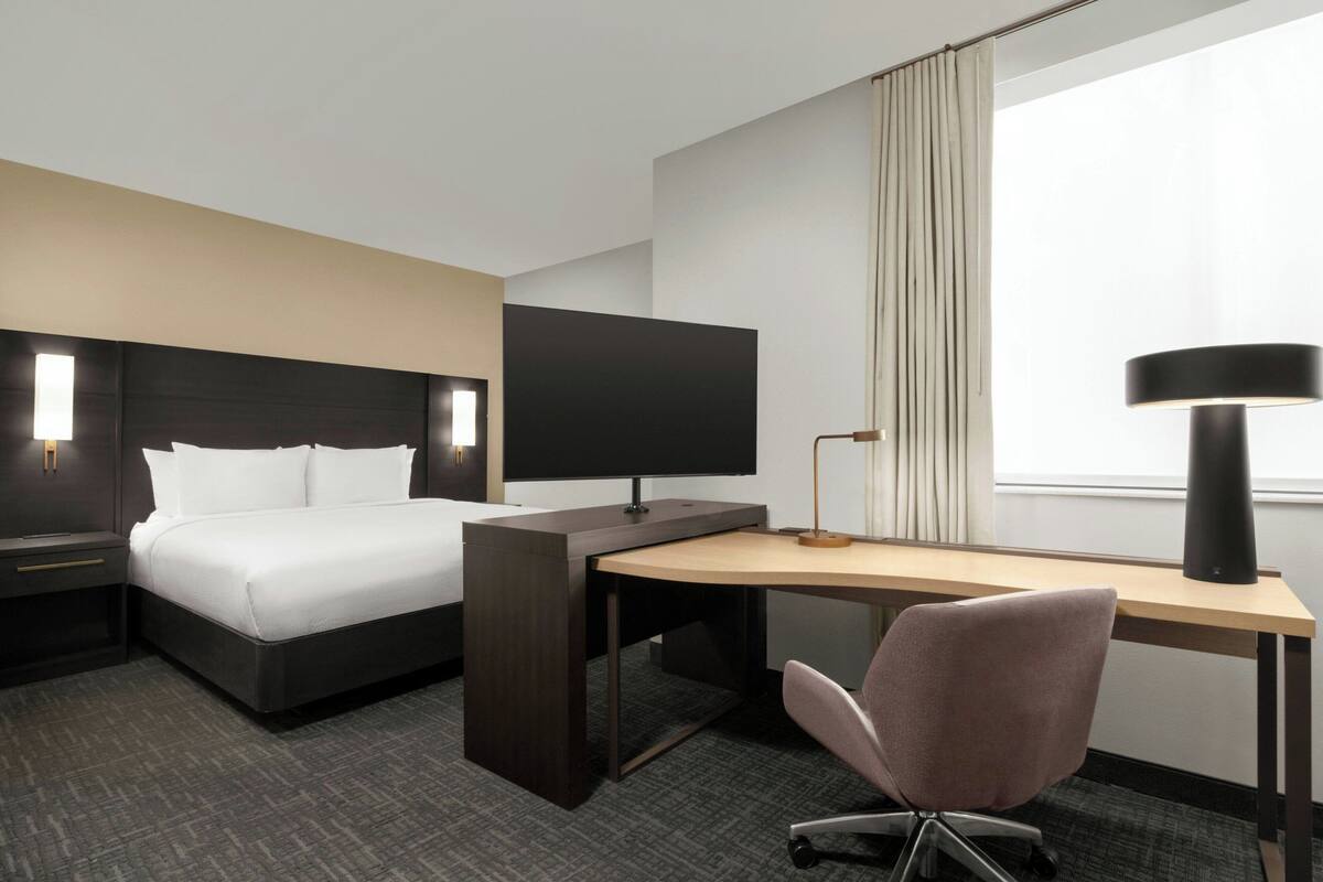 Ett hotellrum med en säng, ett skrivbord, en stol, en tv och en lampa.