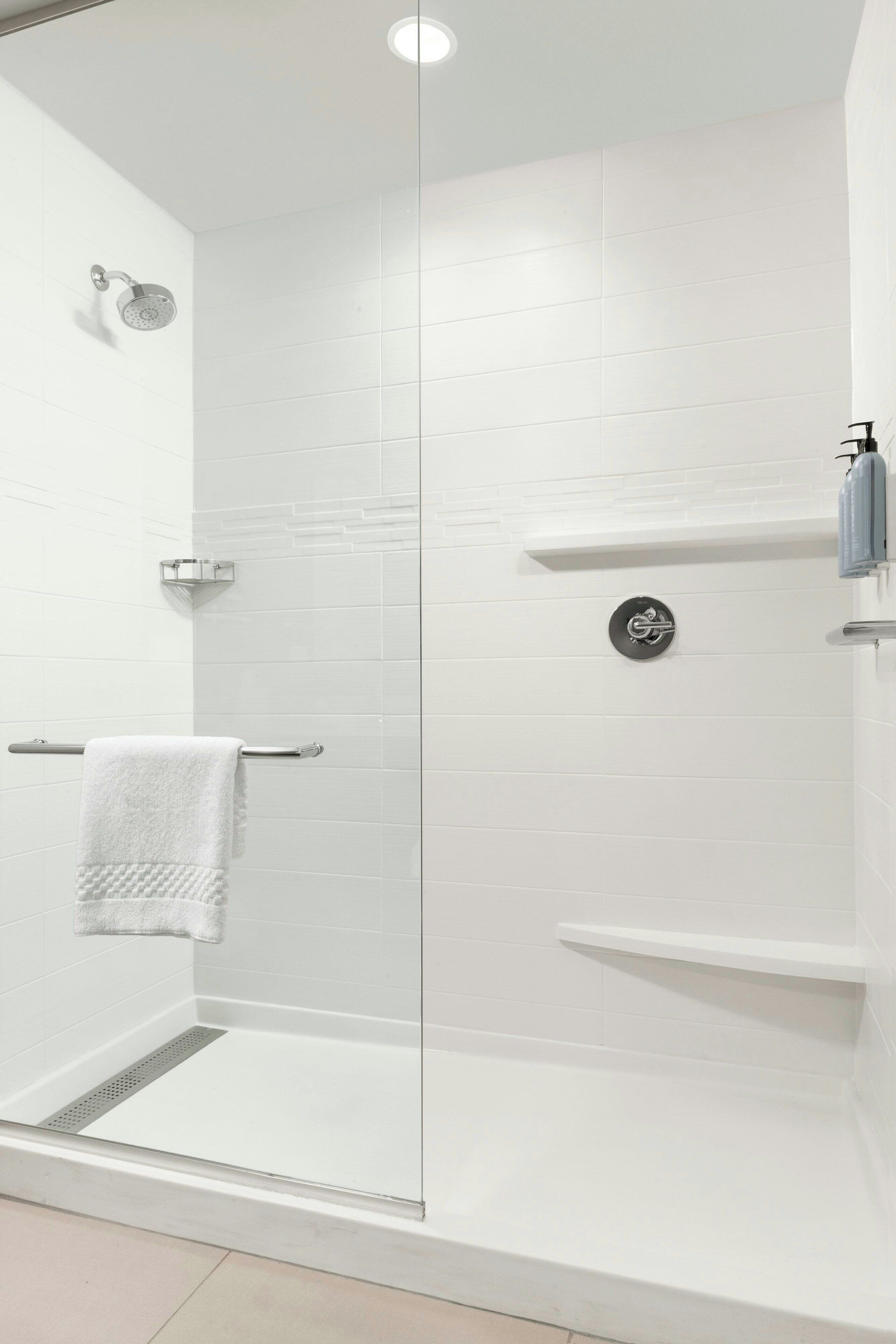 A modern shower area with a glass door, white tiled walls, and a white towel on a metal rack.