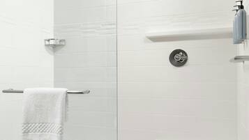 A modern shower area with a glass door, white tiled walls, and a white towel on a metal rack.
