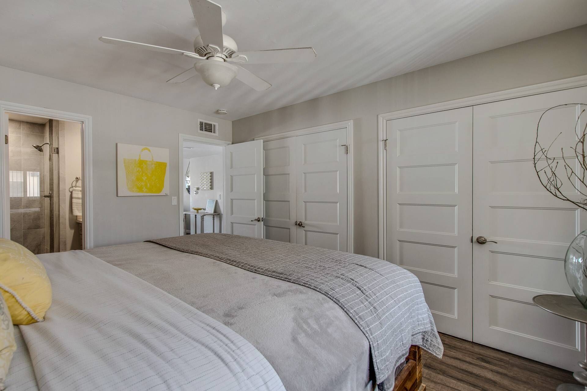 Un dormitorio con cama, ventilador de techo, vestidor y baño con ducha.