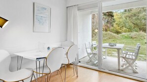A modern dining area with a white table and chairs, a glass partition, and a view of the outdoors. - 1 bedroom cozy apartment in Nexø (Nexø)