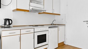 A modern kitchen with white cabinets, a stove, an oven, and a kettle on the countertop. - 1 bedroom cozy apartment in Nexø (Nexø)