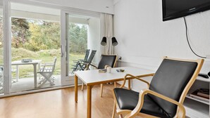 A modern room with a large sliding glass door leading to an outdoor area, a flat-screen TV mounted on the wall, and a table with chairs. - 1 bedroom cozy apartment in Nexø (Nexø)