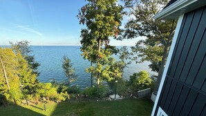 Blick vom Balkon auf einen See, mit einer Rasenfläche und Bäumen im Vordergrund.