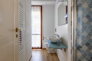 A bathroom with a white sink, a towel hanging on the door, and a shower area with patterned tiles.