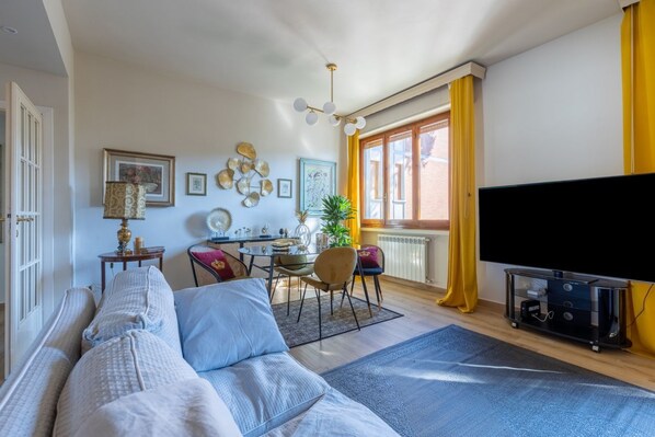 Un salon avec un canapé, une table à manger et des chaises, un téléviseur et une fenêtre avec des rideaux.