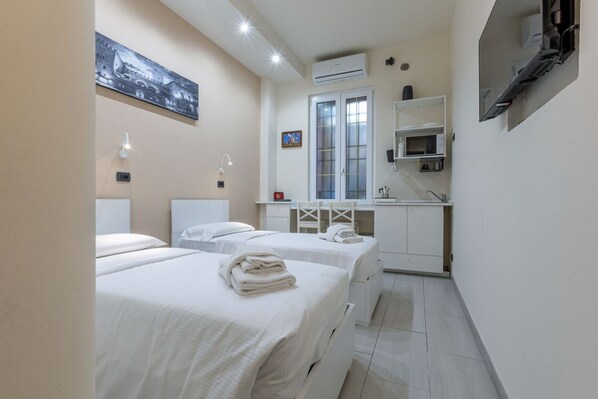 Habitación de hotel con dos camas, una kitchenette pequeña, una ventana con persianas y un cuadro en la pared.