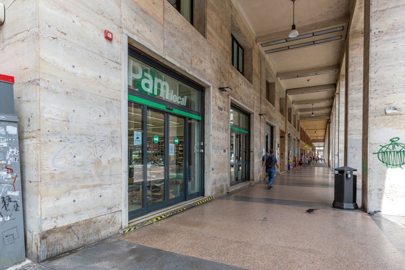 A corridor with a storefront labeled 'pam local' and a trash bin.