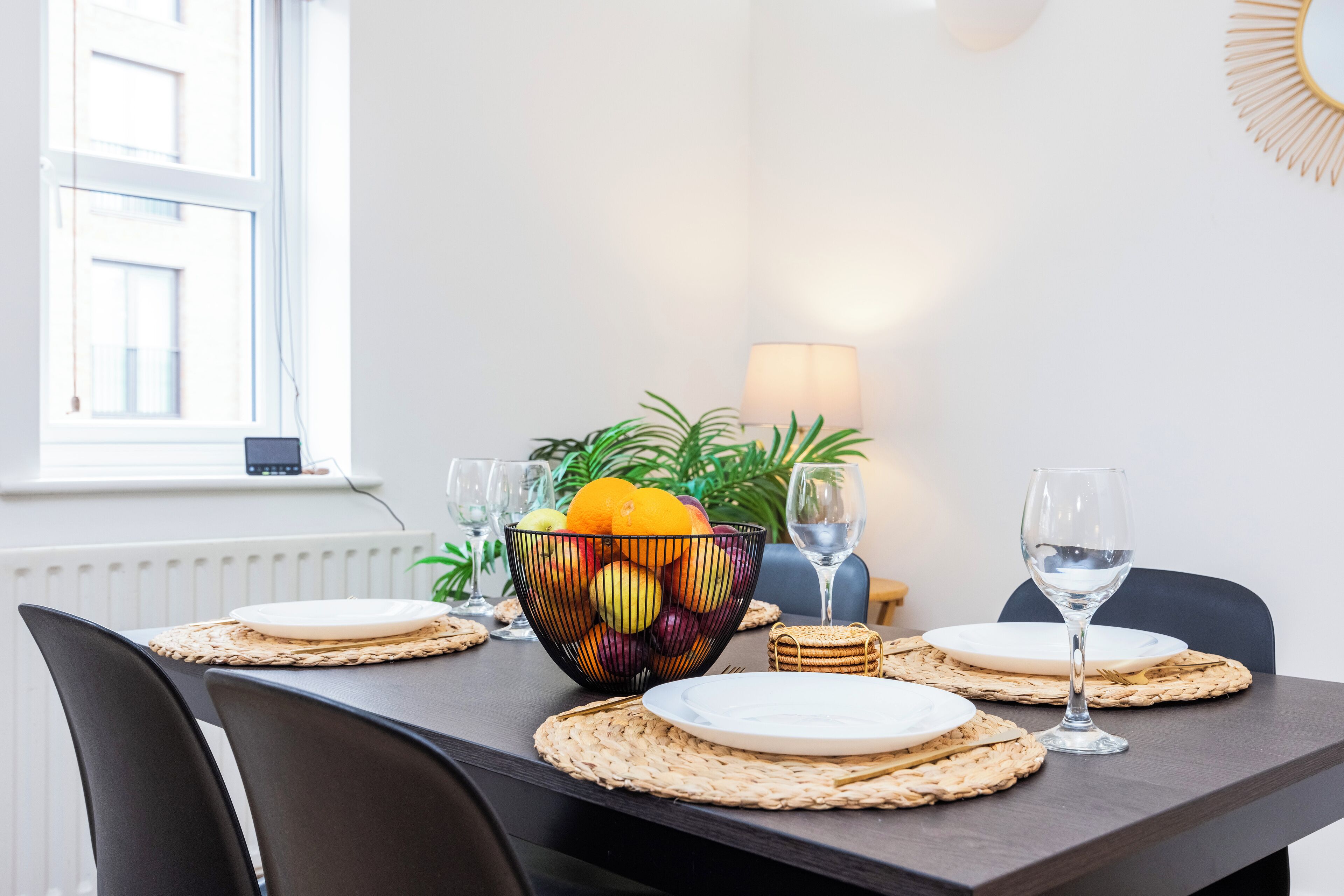 Una mesa de comedor dispuesta con platos, un cuenco de fruta y una copa de vino.
