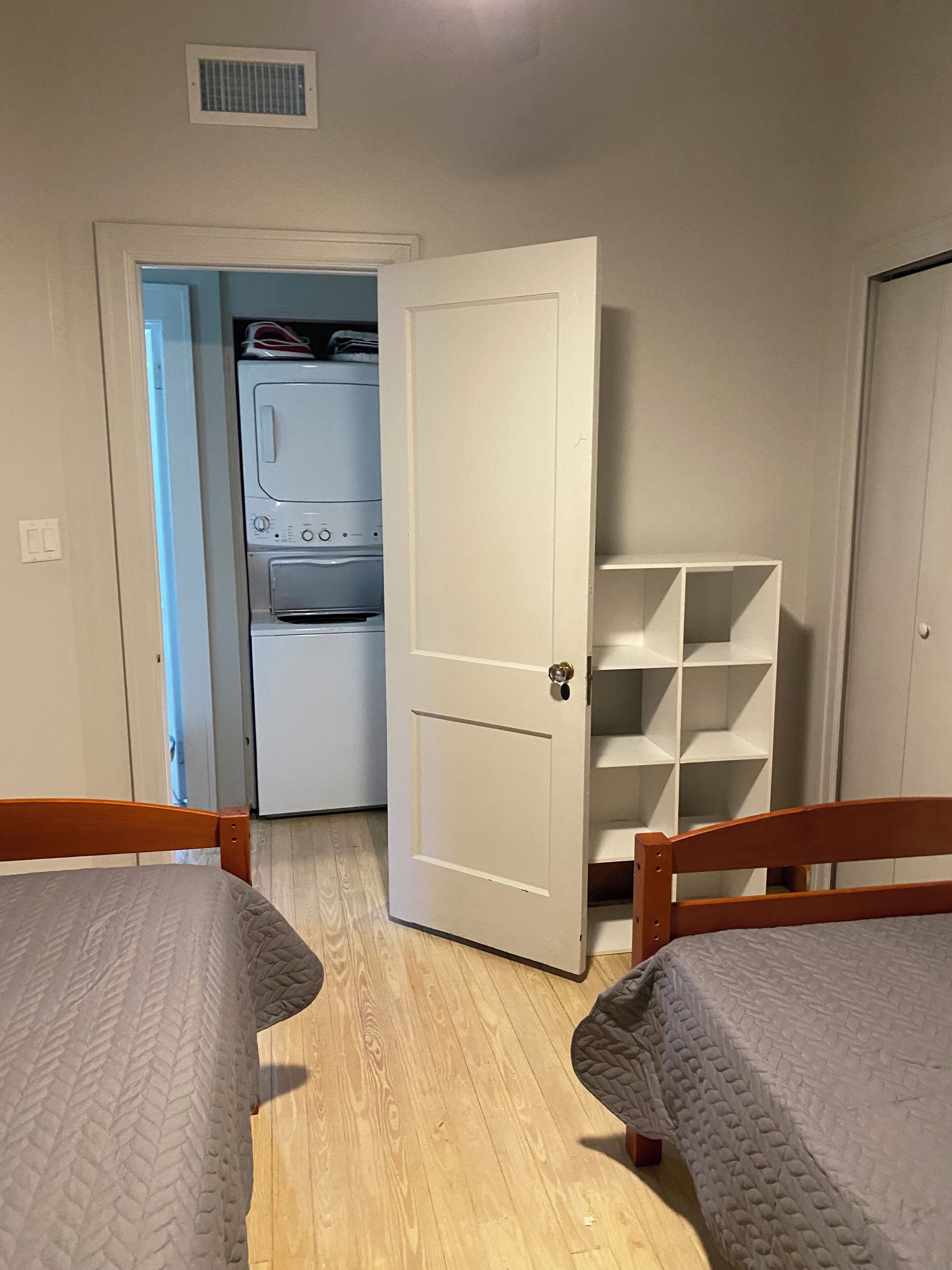 Una habitación con dos camas, un área de lavandería y una puerta blanca.