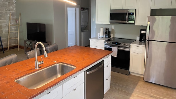 A modern kitchen with white cabinets, a stainless steel refrigerator, a built-in microwave, and a dishwasher. - Eola’s Gem in Downtown Orlando (Orlando)