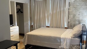 A bedroom with a bed, a desk, a wardrobe, and a brick wall. - Eola’s Gem in Downtown Orlando (Orlando)