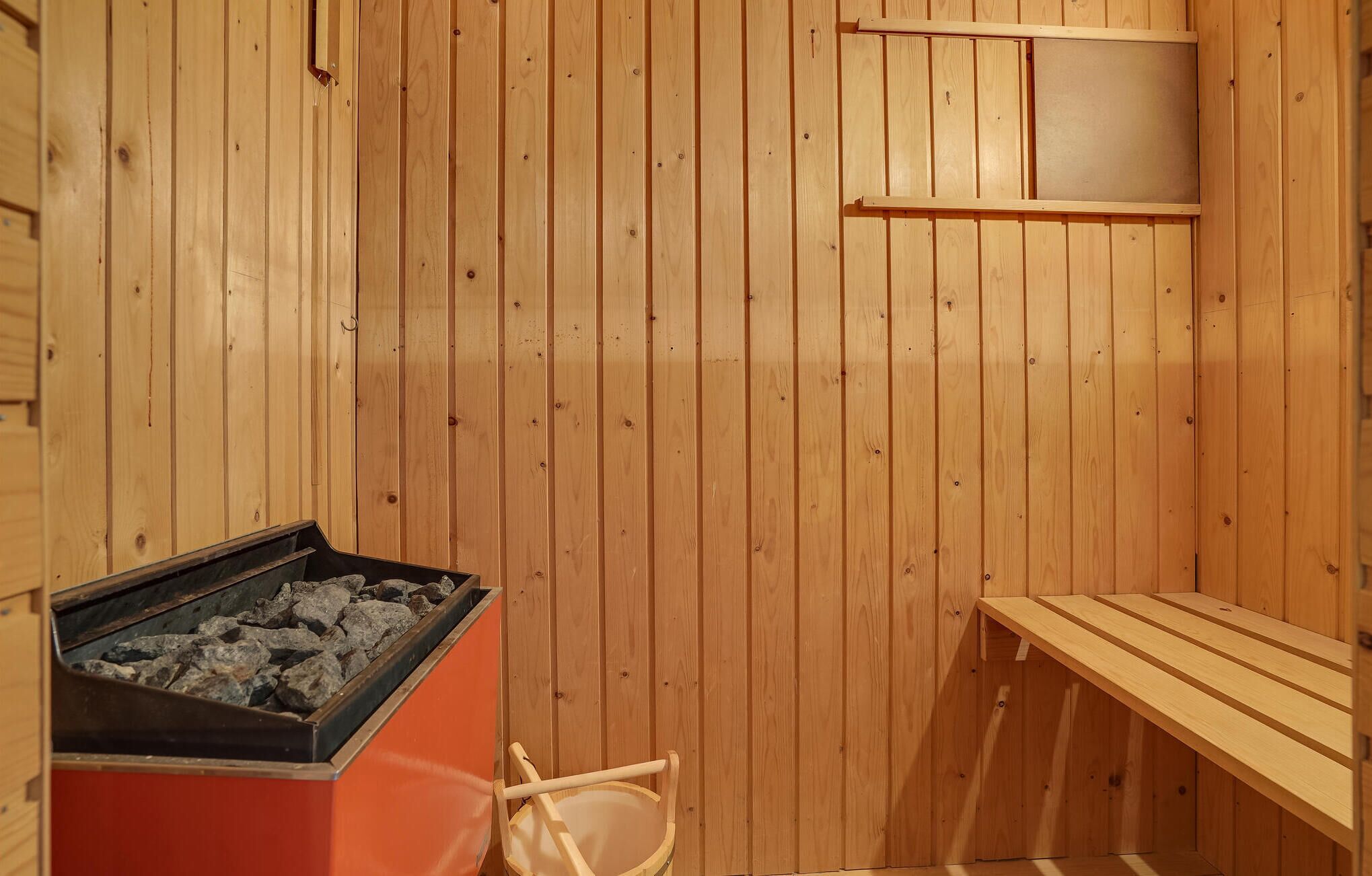 A sauna room with wooden walls, a bench, and a stone-filled container.
