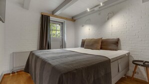 Quarto com cama, janela com cortinas, radiador e parede de tijolos.