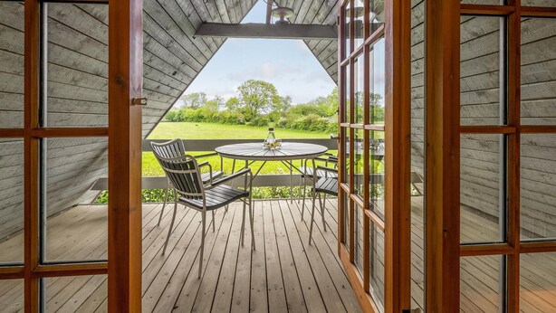 Um deck de madeira com uma mesa redonda e cadeiras, com vista para uma área gramada.