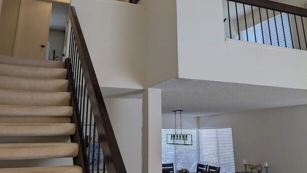A staircase with a black railing, a dining area with a table and chairs, and a chandelier with multiple light fixtures. - Serene & Sunlit Cozy Retreat (Richmond)