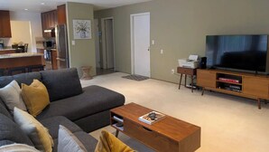 A modern living room with a grey sofa, a wooden coffee table, and a flat-screen TV on a wooden stand. - Serene & Sunlit Cozy Retreat (Richmond)