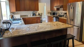 A modern kitchen with wooden cabinets, a granite countertop, a stainless steel refrigerator, and a coffee maker. - Serene & Sunlit Cozy Retreat (Richmond)