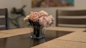 A dining table with a vase of pink flowers, a modern light fixture, and a colorful abstract painting on the wall. - Serene & Sunlit Cozy Retreat (Richmond)