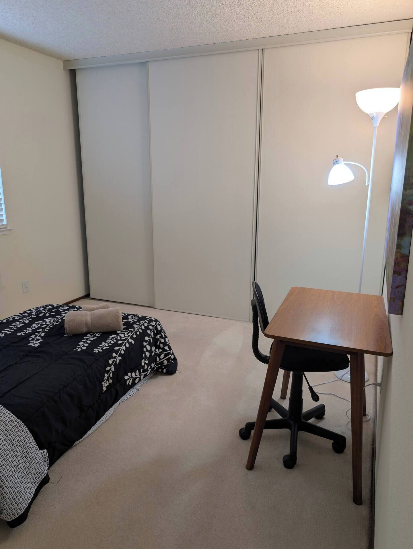 A small, neatly arranged bedroom with a bed, a desk, and a chair.