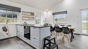 Una cocina moderna con una isla central, zona de comedor con sillas y ventanas grandes que ofrecen vistas al exterior.