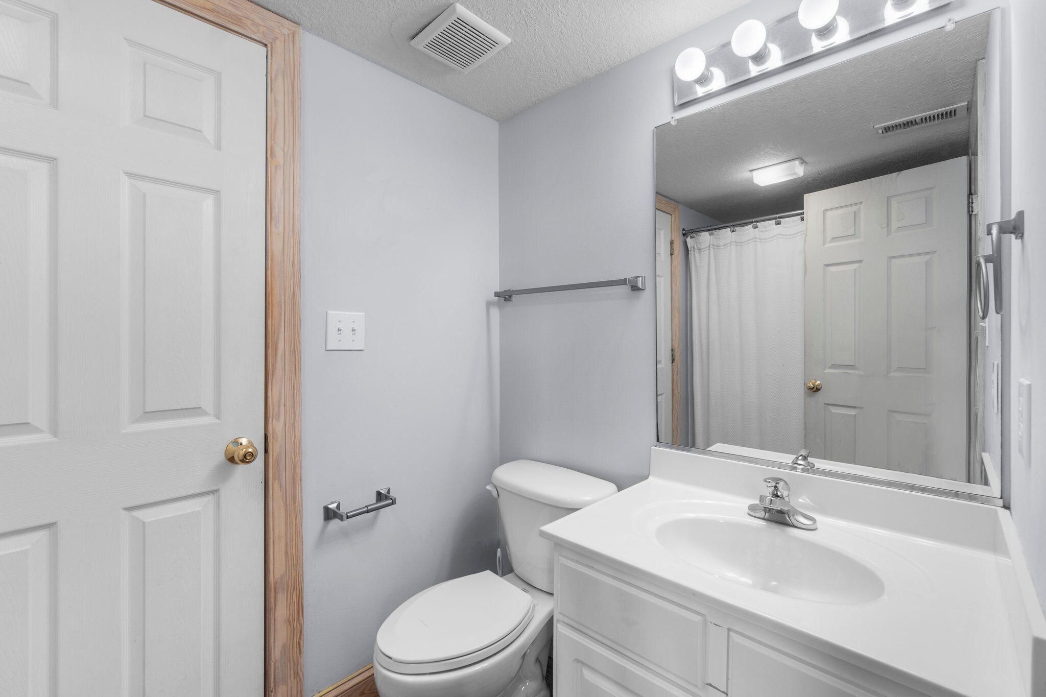 A bathroom with a white toilet, a sink, a mirror, and a shower curtain.
