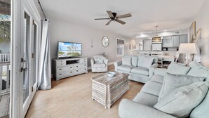 Ein geräumiges Wohnzimmer mit grauem Sofa, Couchtisch, Fernseher und Deckenventilator.