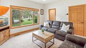 Ein Wohnzimmer mit Ecksofa, Couchtisch und großen Fenstern mit Blick ins Freie.
