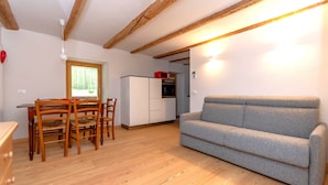 A compact living space with a dining area, kitchenette, and a grey sofa. - Appartamento Focobon (Falcade)