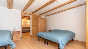 A bedroom with two beds, wooden flooring, and exposed beams. - Appartamento Focobon (Falcade)