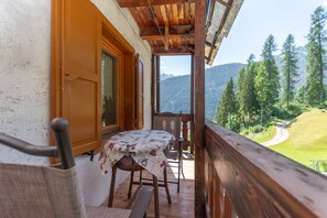A wooden balcony with a table and chairs, overlooking a mountainous landscape. - Appartamento Focobon (Falcade)