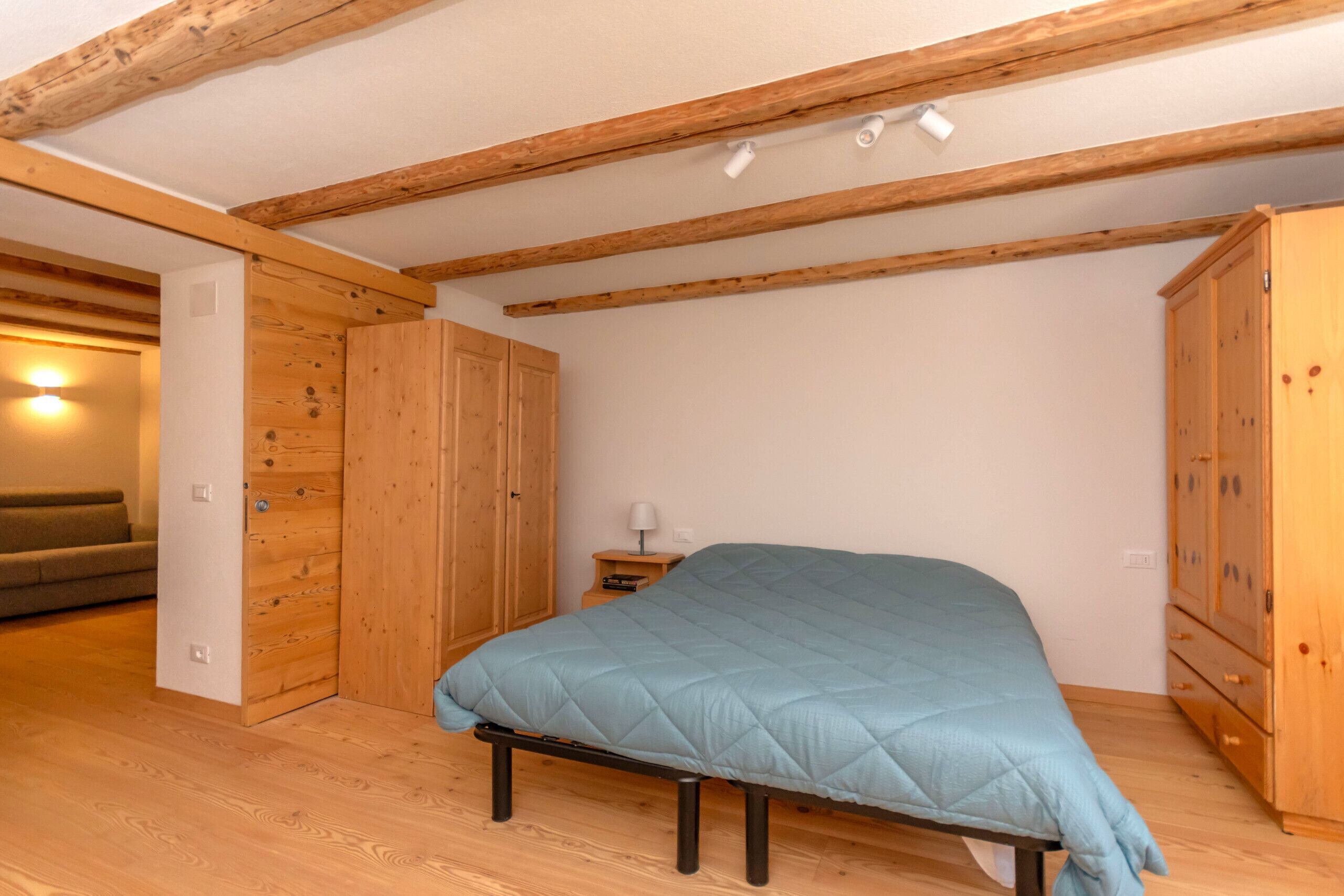 A bedroom with a bed, wooden wardrobe, and a nightstand with a lamp.