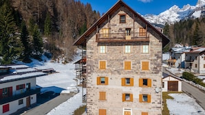 A stone building with multiple windows and balconies, surrounded by snow-covered ground and trees. - Appartamento Focobon (Falcade)