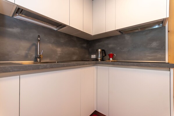 A kitchen with white cabinets, a stainless steel backsplash, and a coffee maker. - Appartamento Focobon (Falcade)