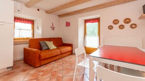 A cozy kitchen with a red table, white chairs, a red and white sofa, and a window with a red curtain. - Casa Alessandra 1 (Falcade)