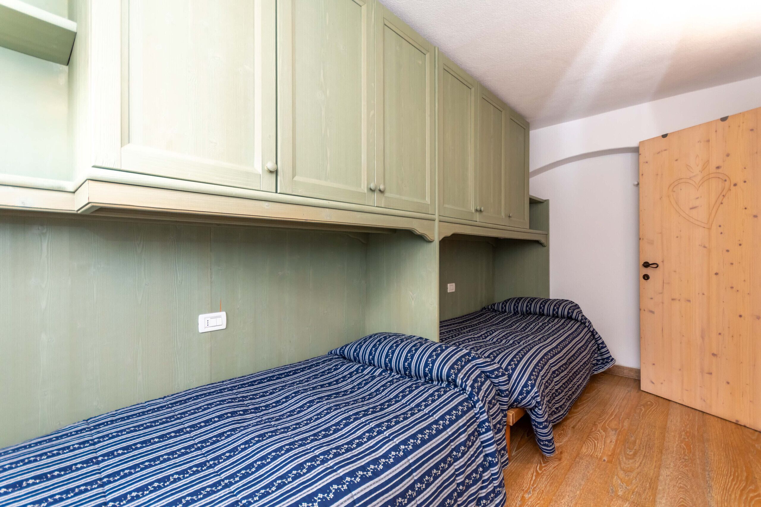 Een studentenkamer met twee eenpersoonsbedden, een houten deur en groene kasten.