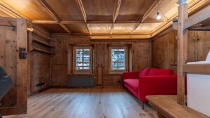 L’intérieur d’un chalet en bois, avec un canapé rouge, des bancs en bois et de grandes fenêtres.