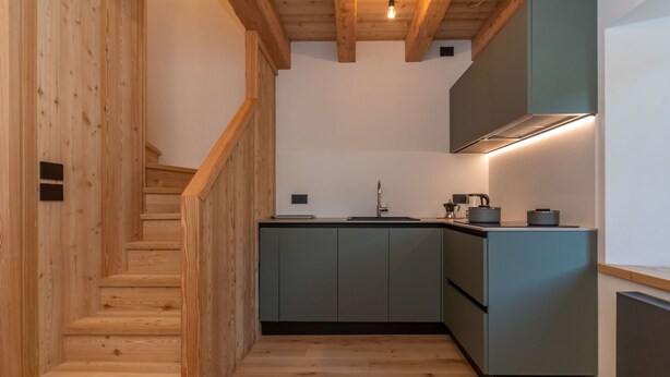 Une cuisine moderne avec un escalier en bois, des meubles gris et une cuisinière encastrée.