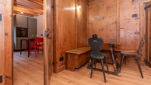 Un intérieur en bois avec un coin repas comprenant un banc et des chaises, une cuisine à l’arrière-plan et une porte en bois.