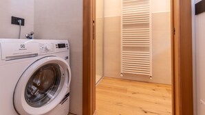 Une petite buanderie équipée d’un lave-linge à chargement frontal, d’une porte en bois et d’un radiateur blanc.
