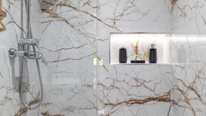A bathroom with a marble wall, a shower with a handheld showerhead, and a shelf with two black bottles. - Cosy new apartment Gueliz (Marrakech)