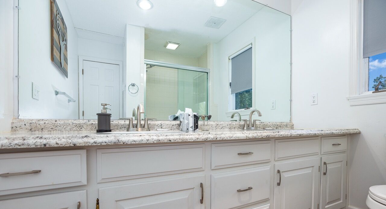 A bathroom with white cabinetry, a large mirror, and a granite countertop.